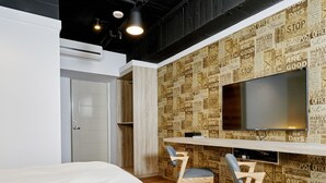 A modern hotel room with a bed, a desk with two chairs, a large TV, and a wall with vintage newspaper print. - Bon Hotel Taipei (Taipei)