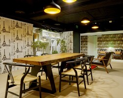 Een vergaderruimte met een lange houten tafel, stoelen en een boekenplank vol boeken.