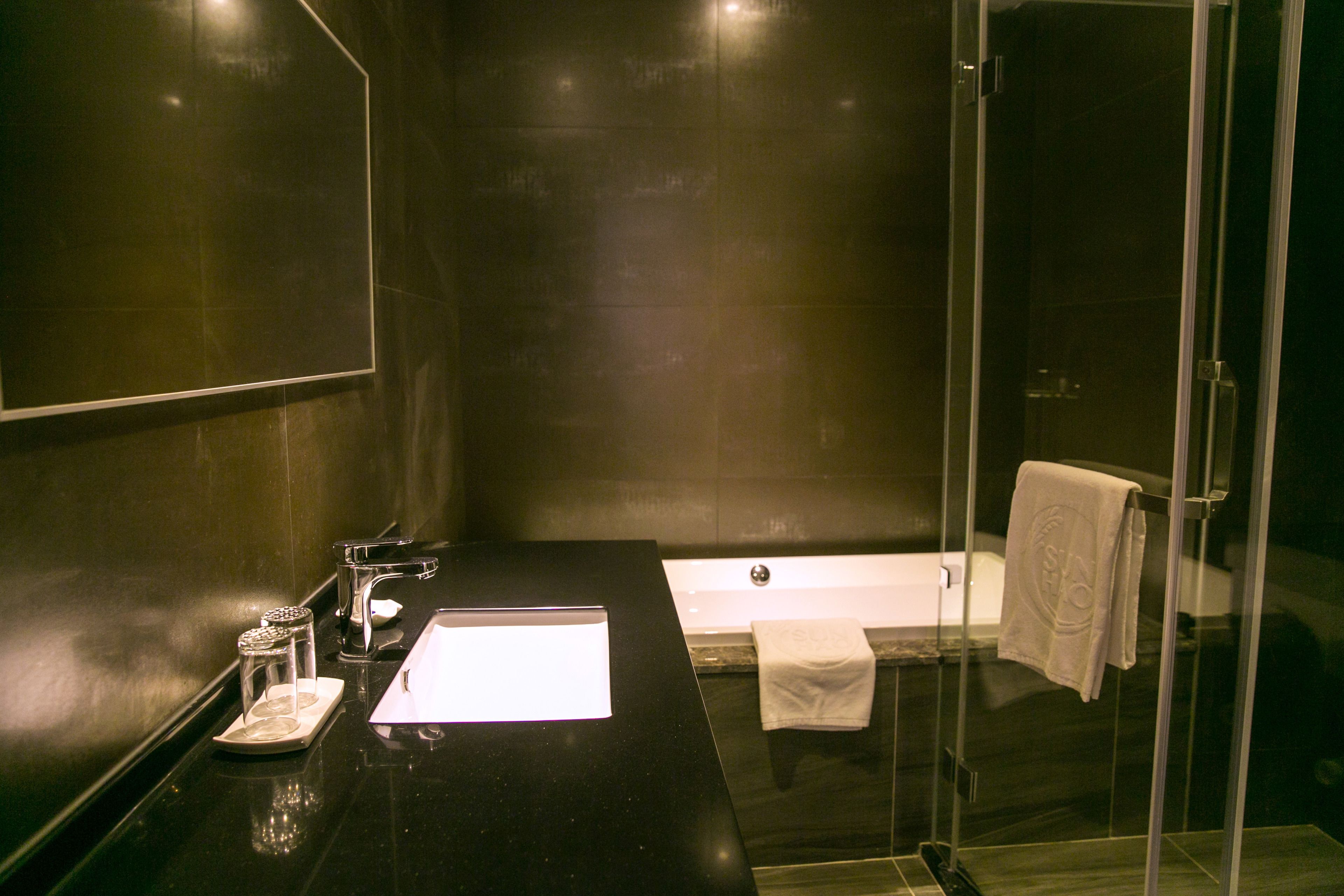A modern bathroom with a black countertop, a glass shower enclosure, and a white bathtub.