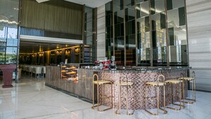 Een moderne bar met een backsplash van mozaïektegels, barstoelen en een aanrecht met een koffieapparaat.