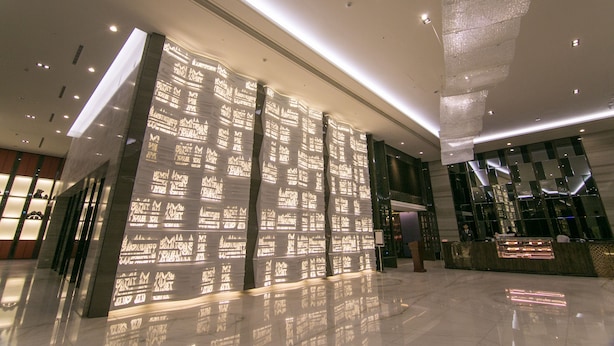 Een moderne lobby met een spiegelende vloer, een receptiebalie en een patroonwand.