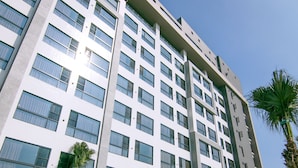 Een modern hotel met een groot zwembadgedeelte, meerdere verdiepingen en palmbomen.