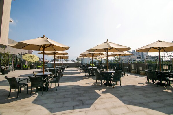 An outdoor patio with multiple tables and chairs, each under a large umbrella. - Sun Hao International Hotel (Douliou)