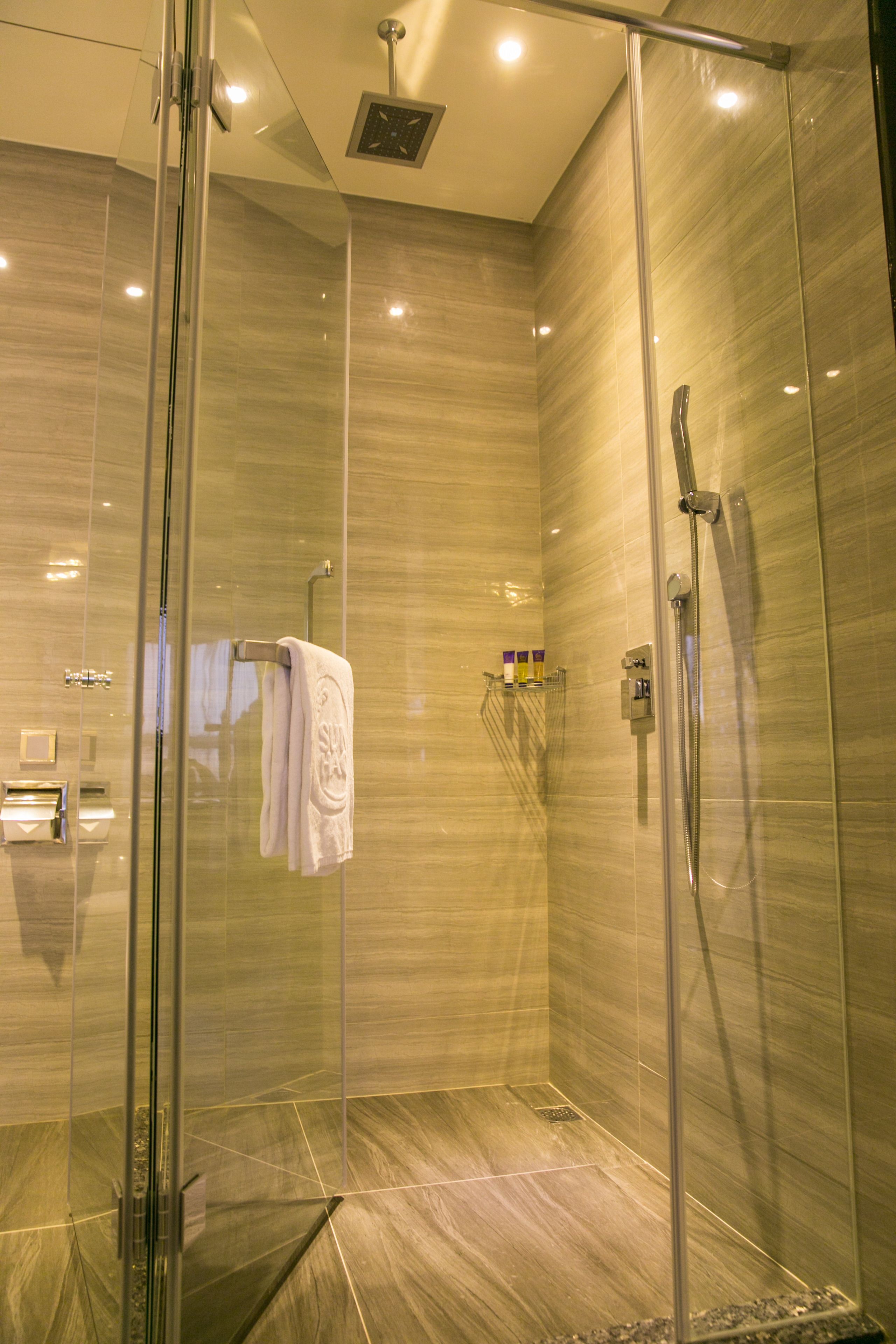 A modern glass-enclosed shower with a handheld showerhead and a wall-mounted faucet.