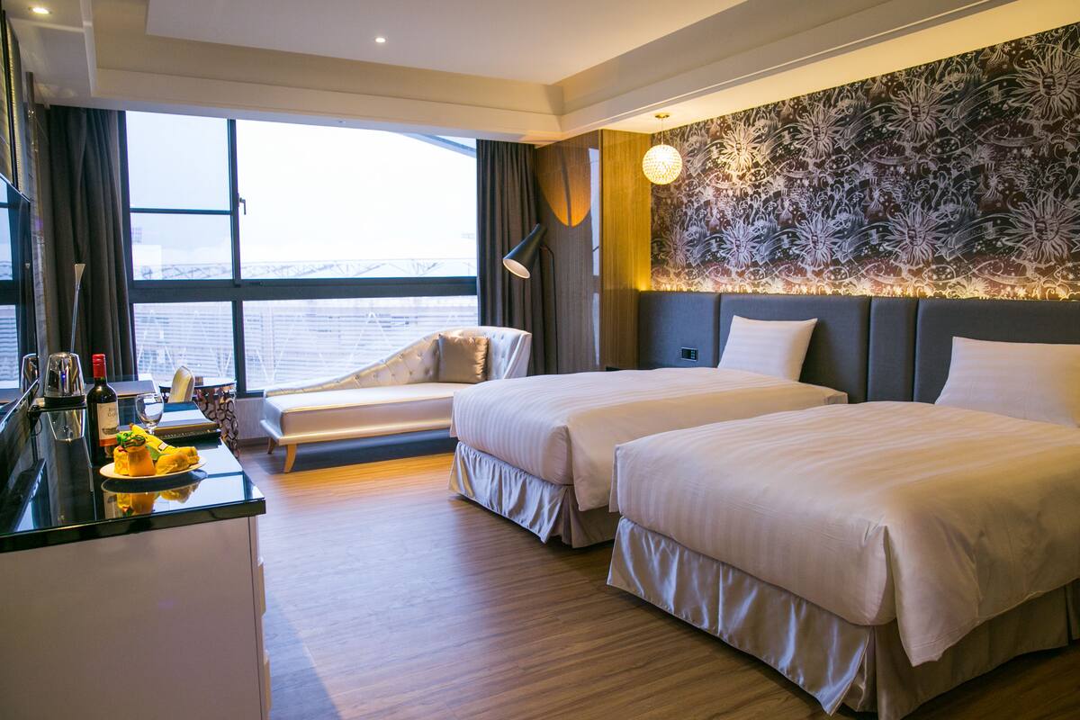 Une chambre d’hôtel avec deux lits, un bureau avec un ordinateur portable, une fenêtre donnant sur la ville et un mur décoratif.
