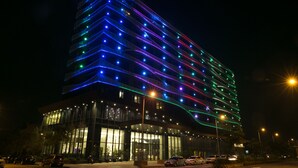 Een modern gebouw met een glazen gevel en meerdere verdiepingen, verlicht met kleurrijke lampen.