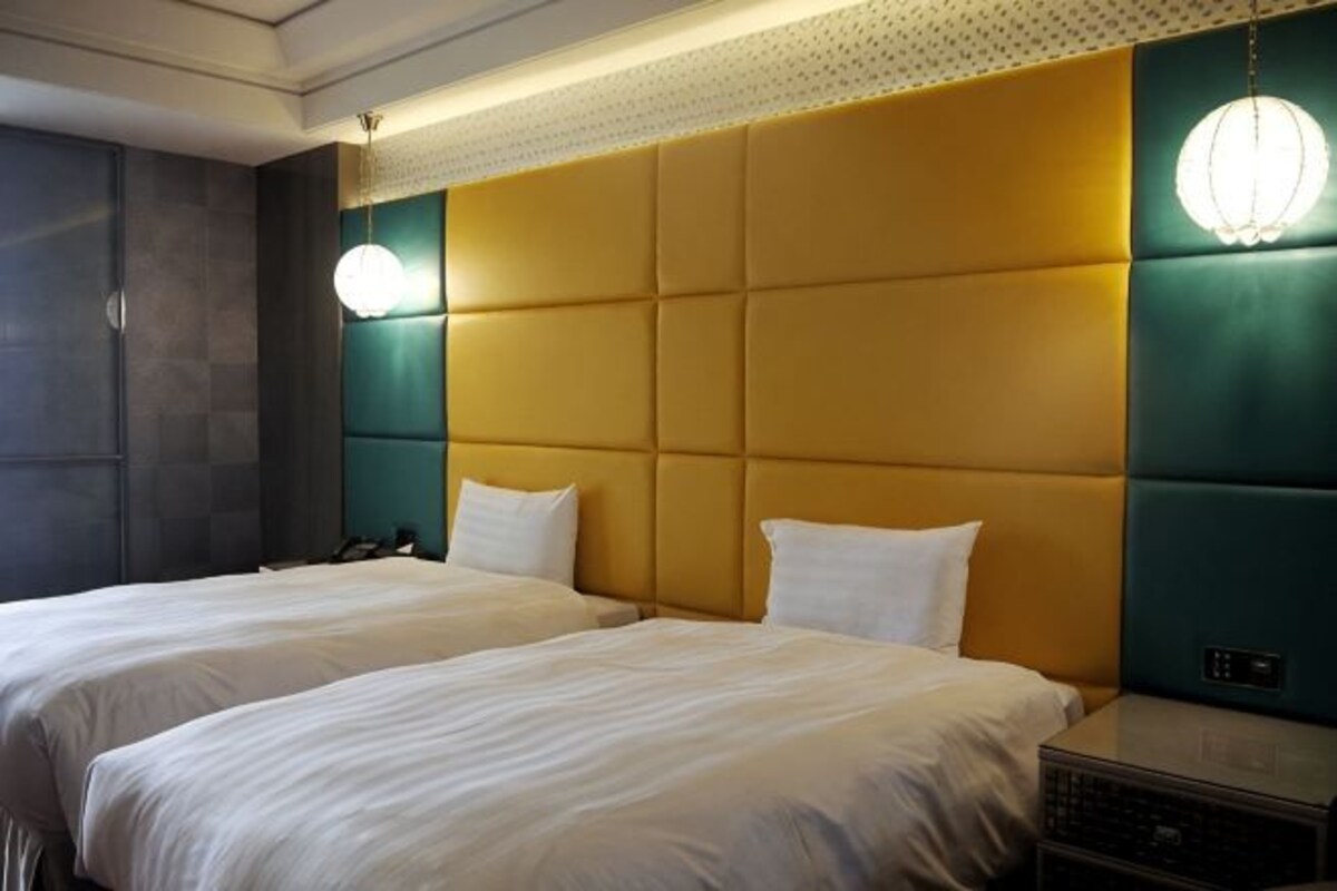 A hotel room with two beds, a large padded headboard, and a modern light fixture.