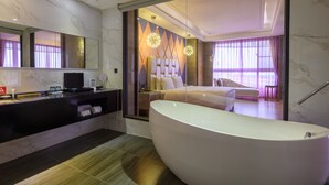 Een moderne badkamer met een groot bad, een wastafel met spiegel, en een bed in de aangrenzende kamer.