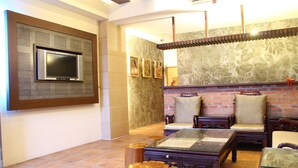 A living room with a TV mounted on the wall, wooden furniture, and a brick fireplace. - Constellation Coast B&B (Hualien City)