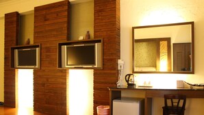 A hotel room with wooden panel walls, two TVs mounted on the wall, a desk with a coffee maker, a chair, and a small refrigerator. - Constellation Coast B&B (Hualien City)