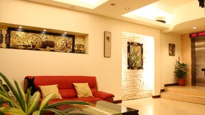 A modern lobby with a red sofa, a glass coffee table, and a decorative wall with artwork. - Constellation Coast B&B (Hualien City)