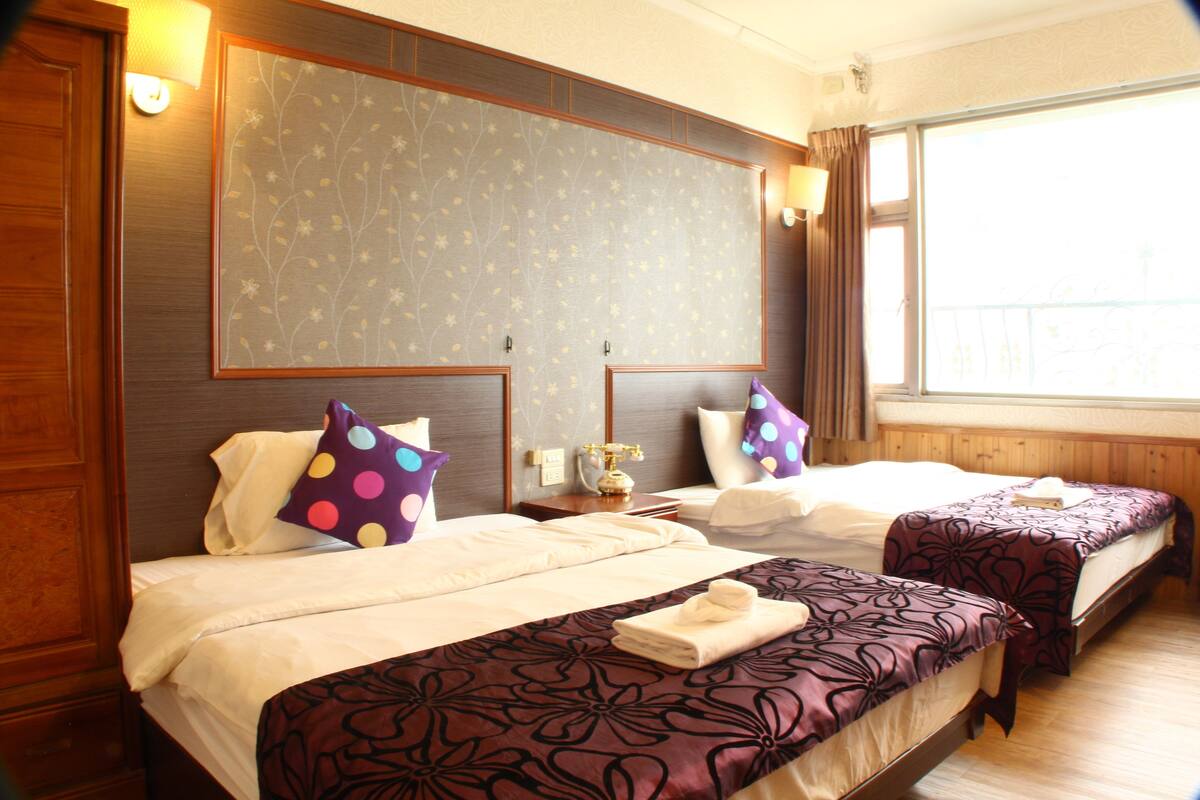 A hotel room with two beds, a large window, and a wooden headboard.