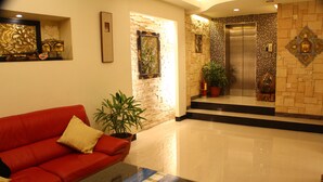 A lobby with a red sofa, a glass coffee table, a potted plant, and an elevator. - Constellation Coast B&B (Hualien City)