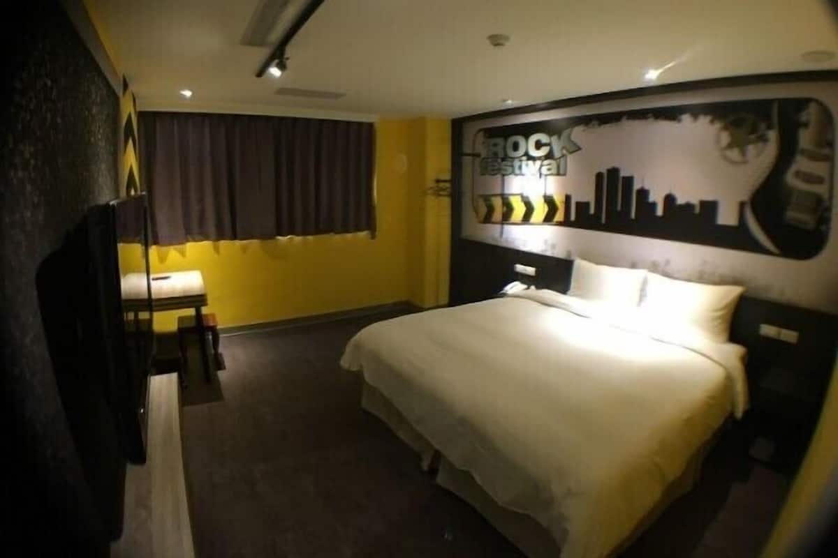 Una habitación de hotel con una cama, una mesita de noche, un espejo y una pared con un cartel que dice 'Rock Festival'.