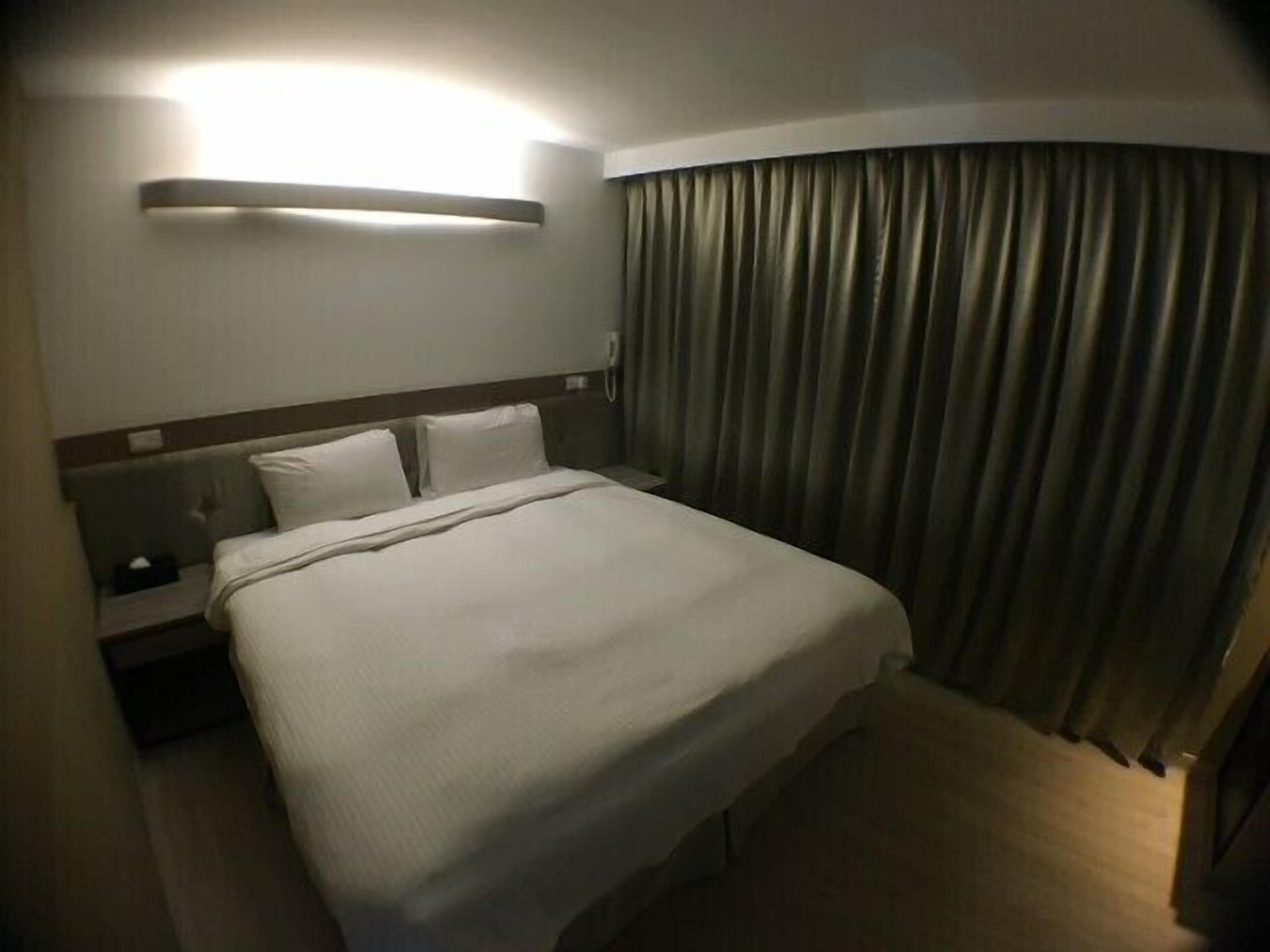 Une chambre d’hôtel avec un lit bien fait, une table de chevet et un rideau.