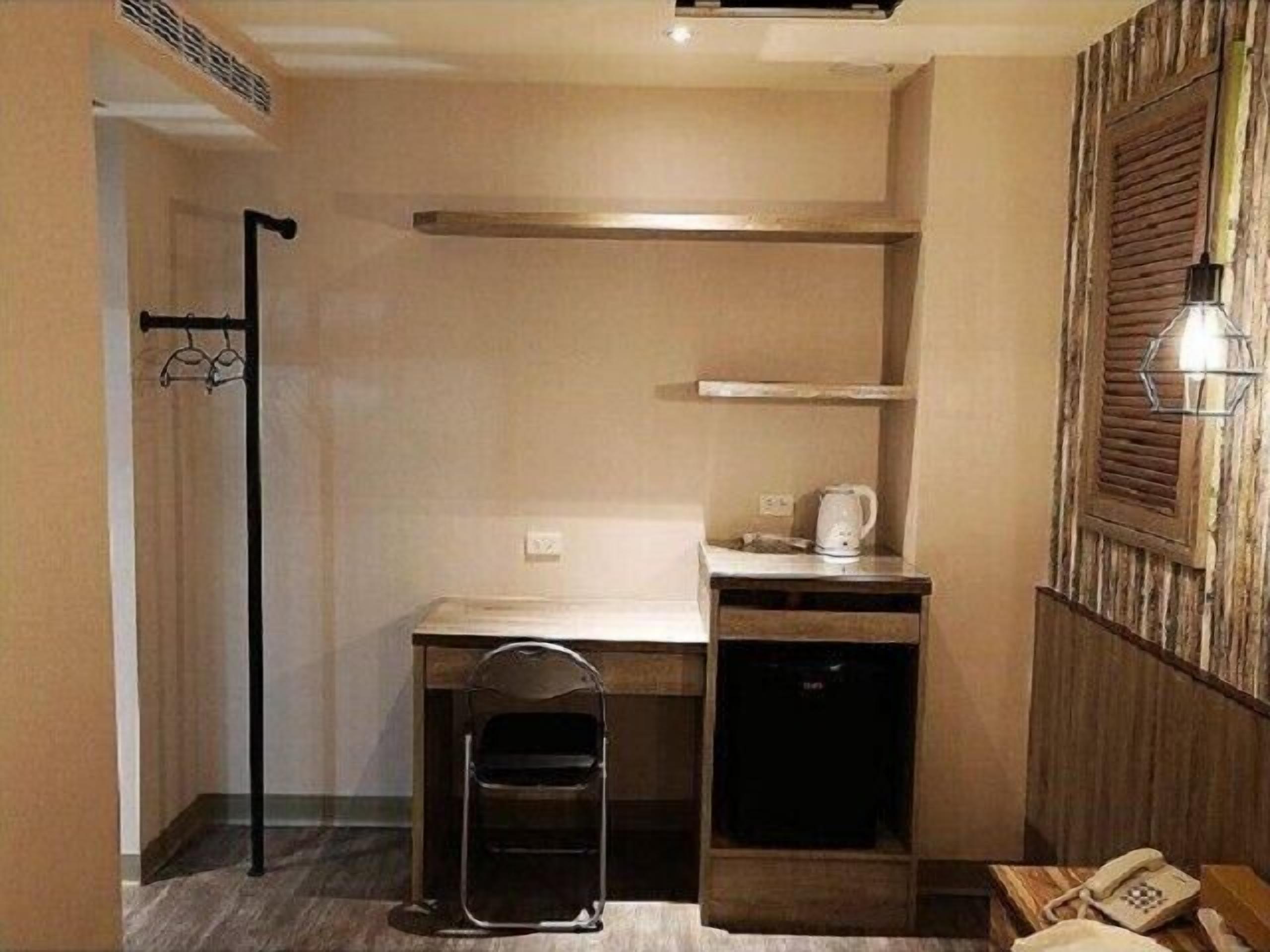 Une pièce de taille modeste, comprenant un bureau, une chaise, un petit meuble, une poubelle et un téléphone fixé au mur.