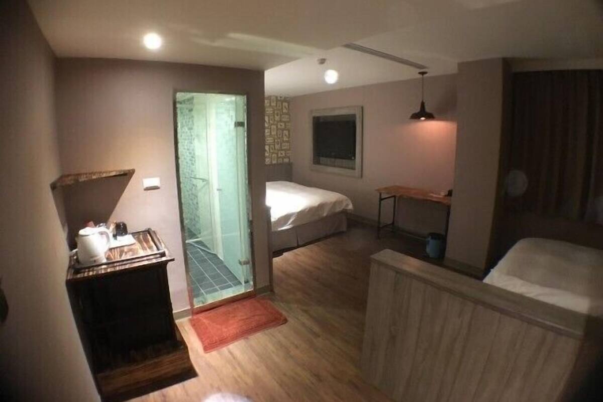 Habitación de hotel compacta con ducha, cama, escritorio pequeño y mesita de noche.