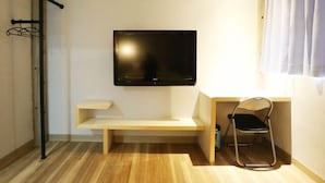A small, modern room with a flat-screen TV mounted on the wall, a wooden bench, a desk, and a chair.