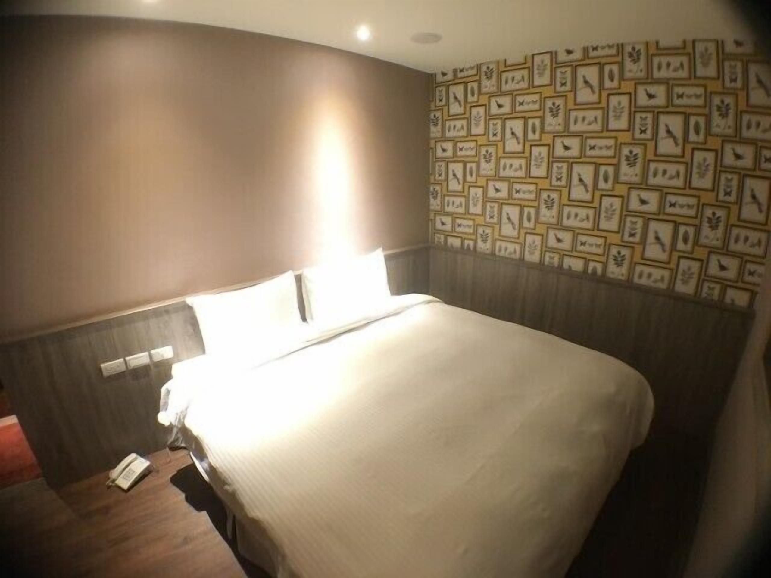 Une chambre d’hôtel avec un grand lit, un mur orné de tableaux et un téléphone posé sur le sol.