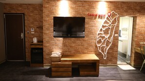 A hotel room with a brick wall, a flat-screen TV mounted above a wooden console table, a basket on the console, and a map decoration.