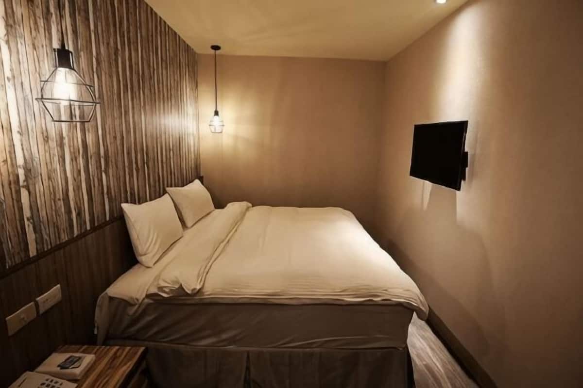 Habitación de hotel con cama, pared de paneles de madera, televisor montado y teléfono junto a la cama.