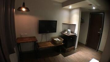 A small, dimly lit room with a wooden bench, a television mounted on the wall, a small cabinet, and a door.