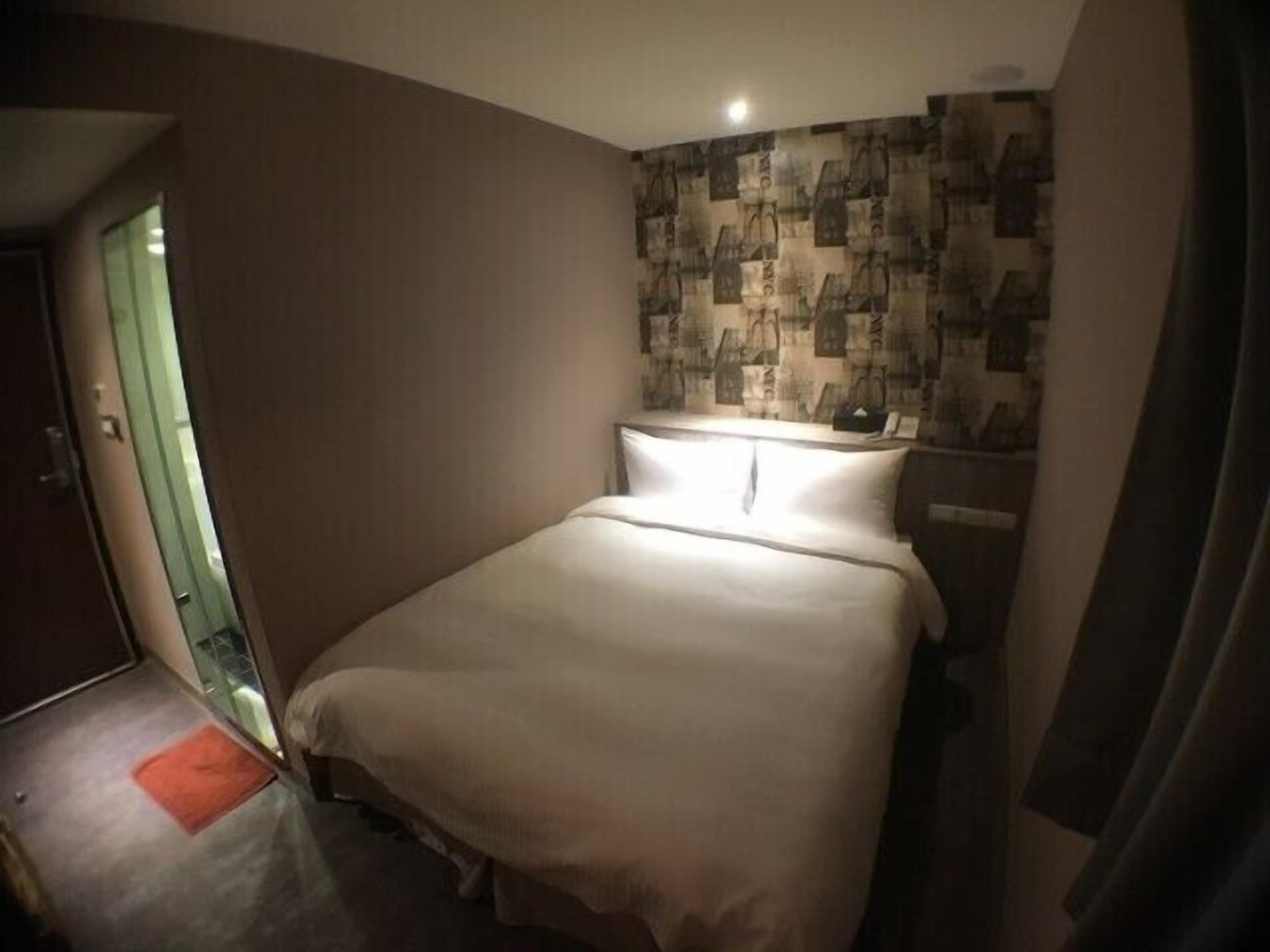 A hotel room with a single bed, a small bedside table, and a wall with a patterned wallpaper.