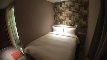 A hotel room with a single bed, a small bedside table, and a wall with a patterned wallpaper.