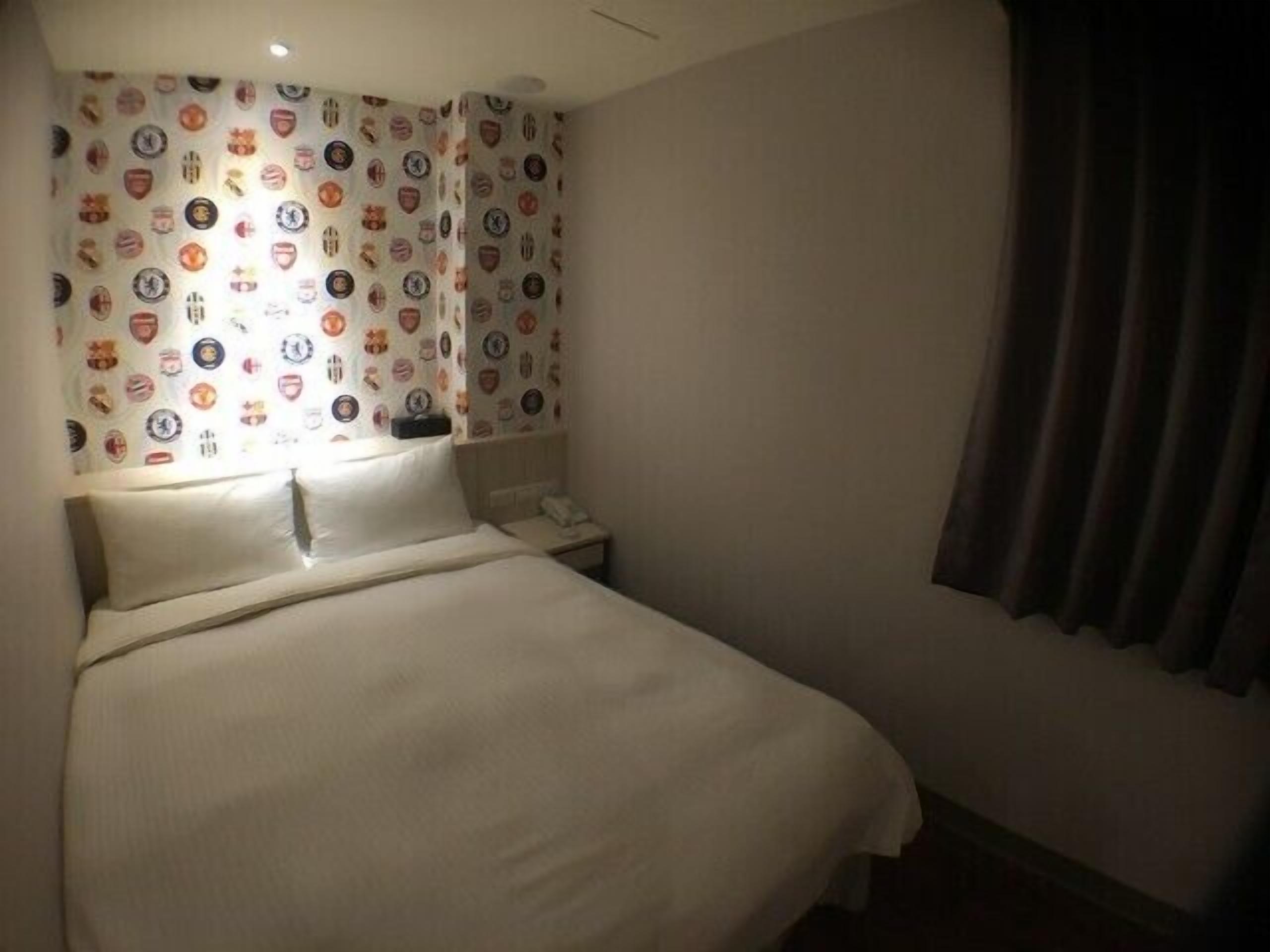 Une chambre d’hôtel avec un lit, une table de chevet, un téléphone et un rideau.