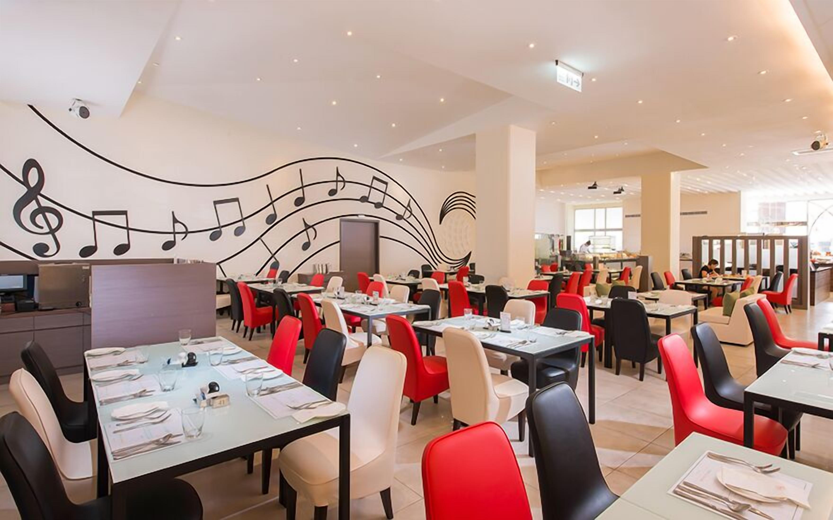 A spacious restaurant with tables and chairs, a large mural with musical notes, and a modern interior design.
