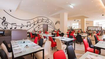 A spacious restaurant with tables and chairs, a large mural with musical notes, and a modern interior design.