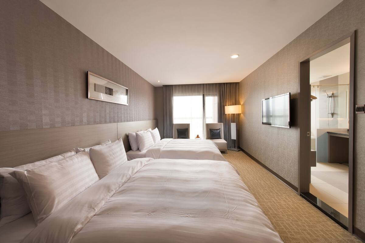 A hotel room with two beds, a TV, a mirror, and a bathroom visible through an open door.
