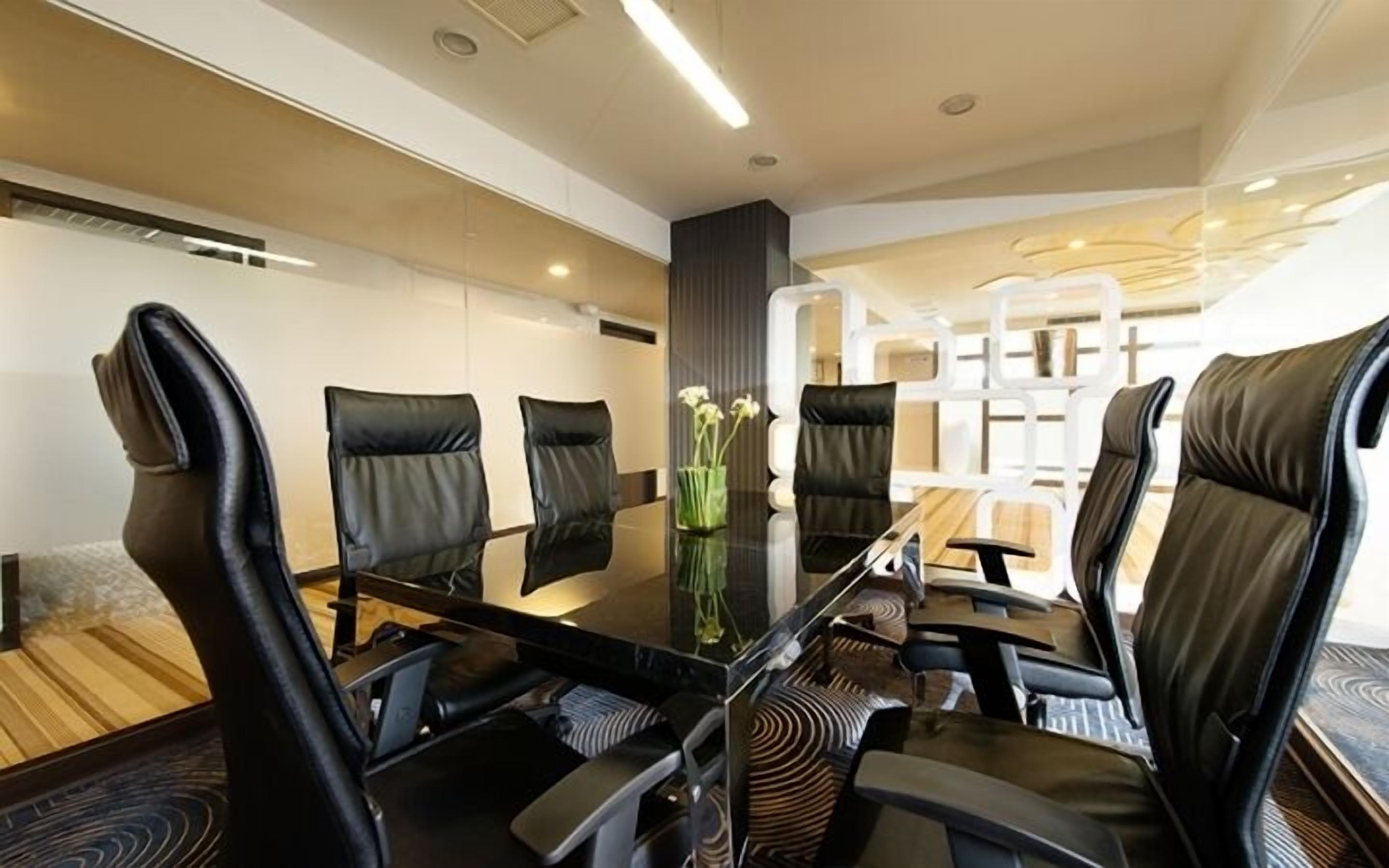 Un salón de conferencias con una mesa de vidrio, sillas de cuero negro y un jarrón con flores blancas.