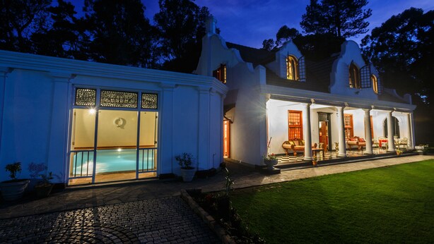 Un edificio blanco con piscina, terraza techada y césped bien cuidado.