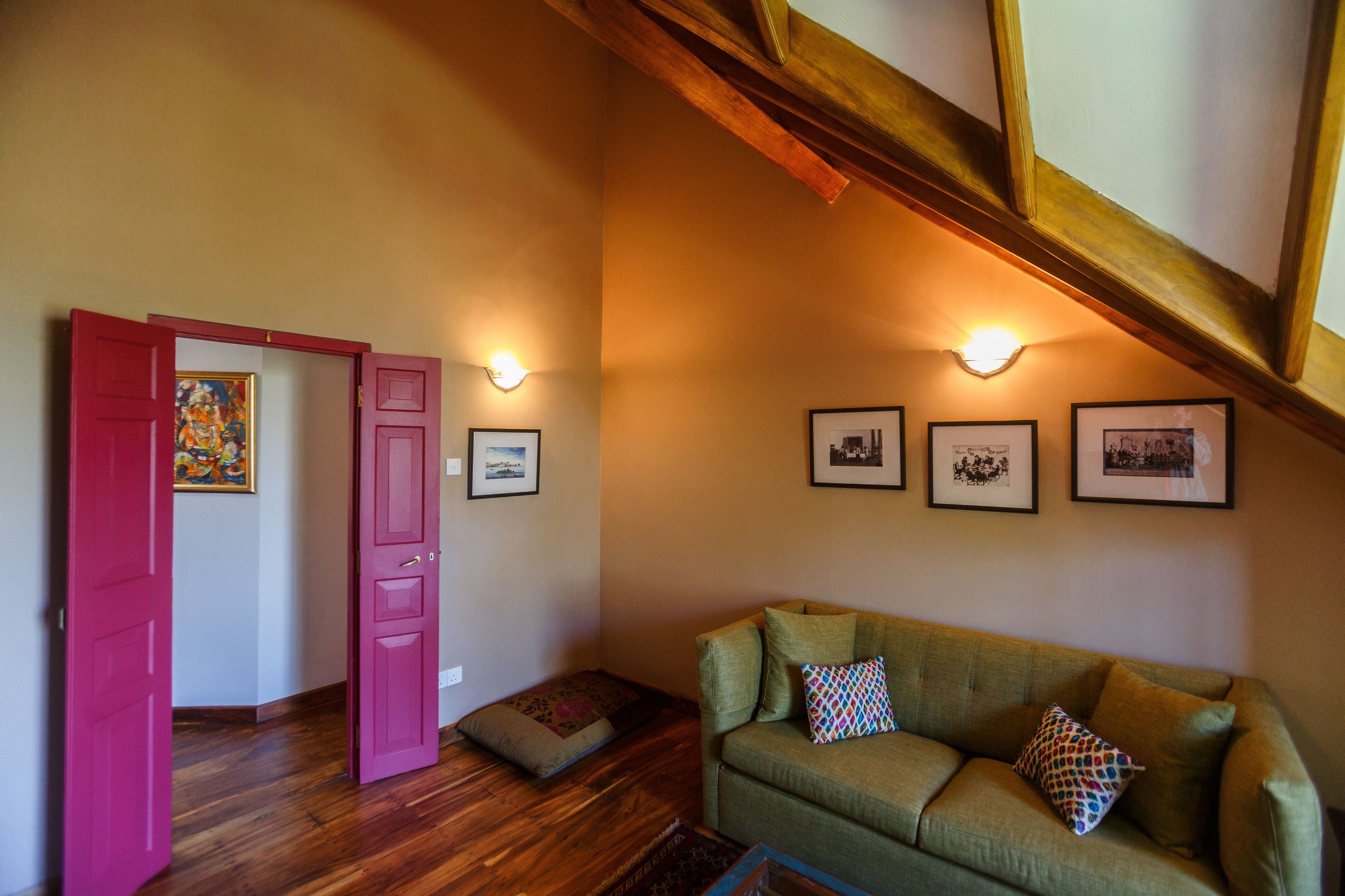 A room with a green sofa, a red door, wooden flooring, and wall-mounted lights.