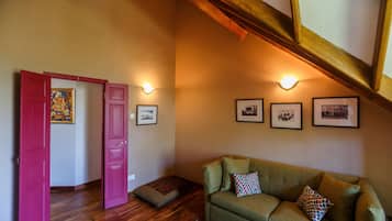 A room with a green sofa, a red door, wooden flooring, and wall-mounted lights.