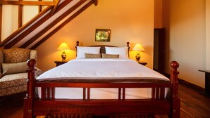 Un dormitorio con una cama de madera, dos lámparas de noche, un cuadro en la pared y un sillón estampado.