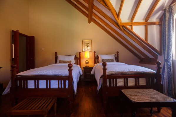 A bedroom with two wooden beds, a bench, a nightstand with a lamp, and a framed picture on the wall.