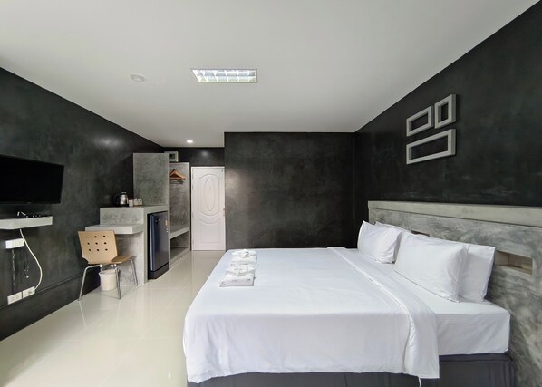 A modern hotel room with a large bed, a flat-screen TV, a wardrobe, and a small seating area.