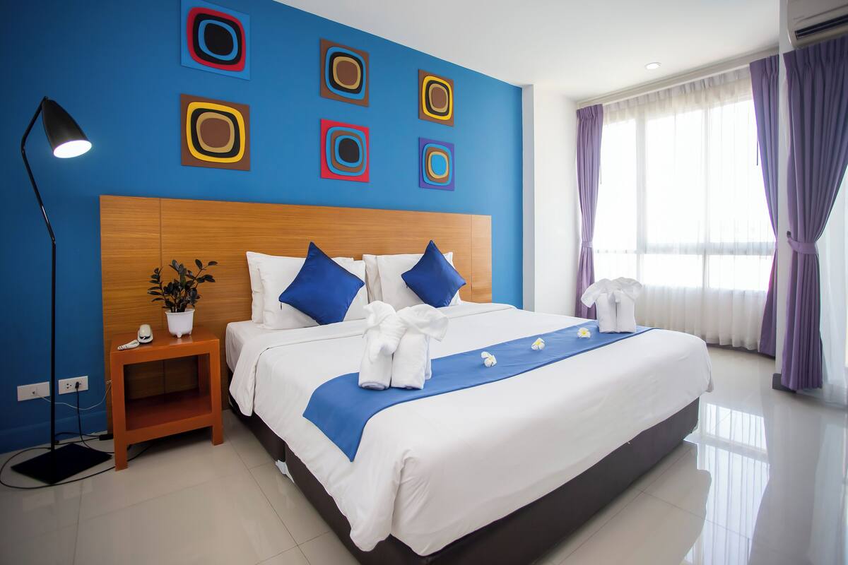 Une chambre d’hôtel avec un grand lit, une table de chevet avec une lampe et un mur orné d’œuvres d’art géométriques aux couleurs vives.