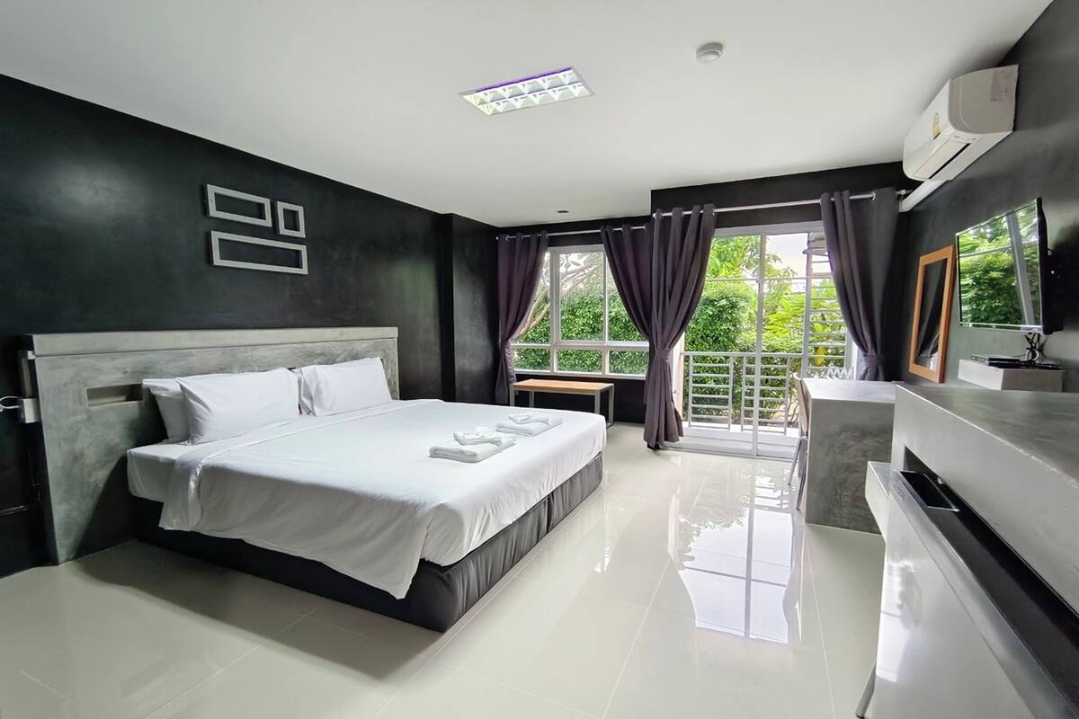 Une chambre d’hôtel moderne avec un grand lit, une table de chevet, un miroir et une fenêtre avec des rideaux.