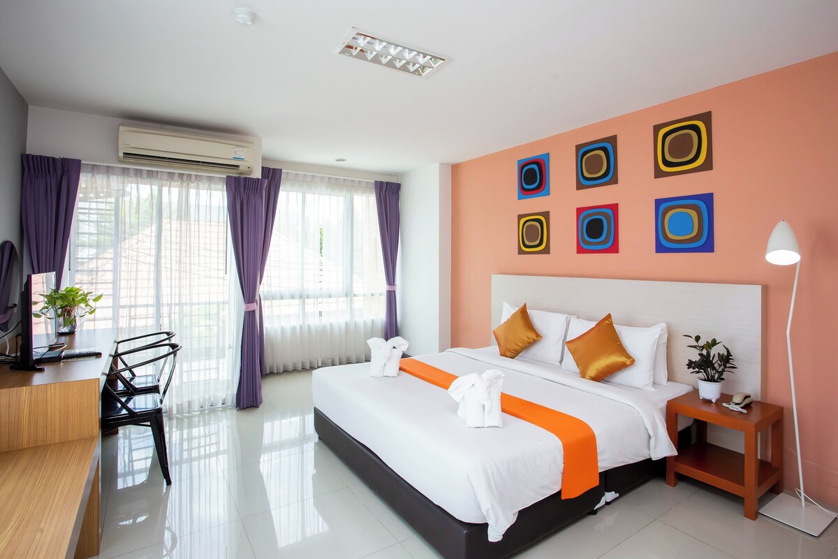 Una habitación de hotel con cama, mesita de noche, escritorio, silla y cortinas.