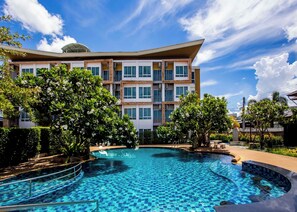 A modern hotel with a swimming pool, surrounded by lush greenery and a clear blue sky. - Nano Place Hotel (Si Racha)