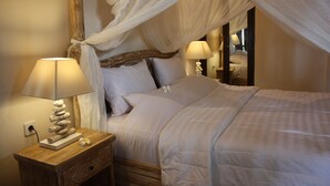 A bedroom with a canopy bed, bedside lamps, a wooden nightstand, and a decorative lamp. - Joglo on the Beach (Banjar)