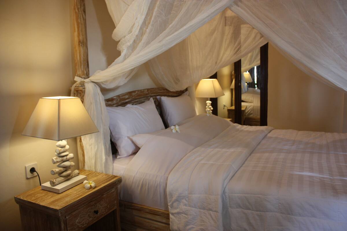 A bedroom with a canopy bed, bedside lamps, a wooden nightstand, and a decorative lamp.
