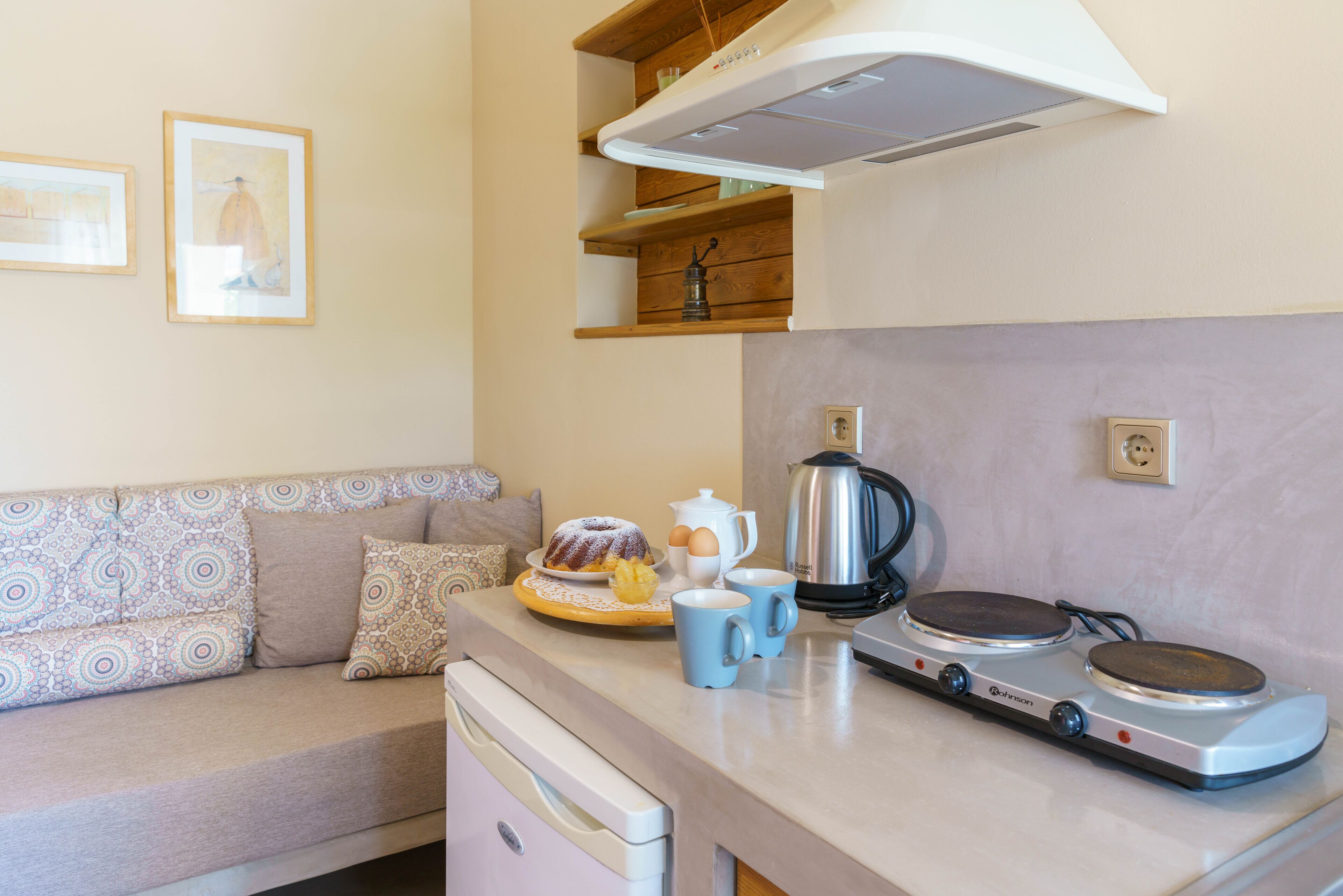 Una kitchenette con estufa, cafetera y una pequeña mesa de comedor con un pastel y tazas de café.