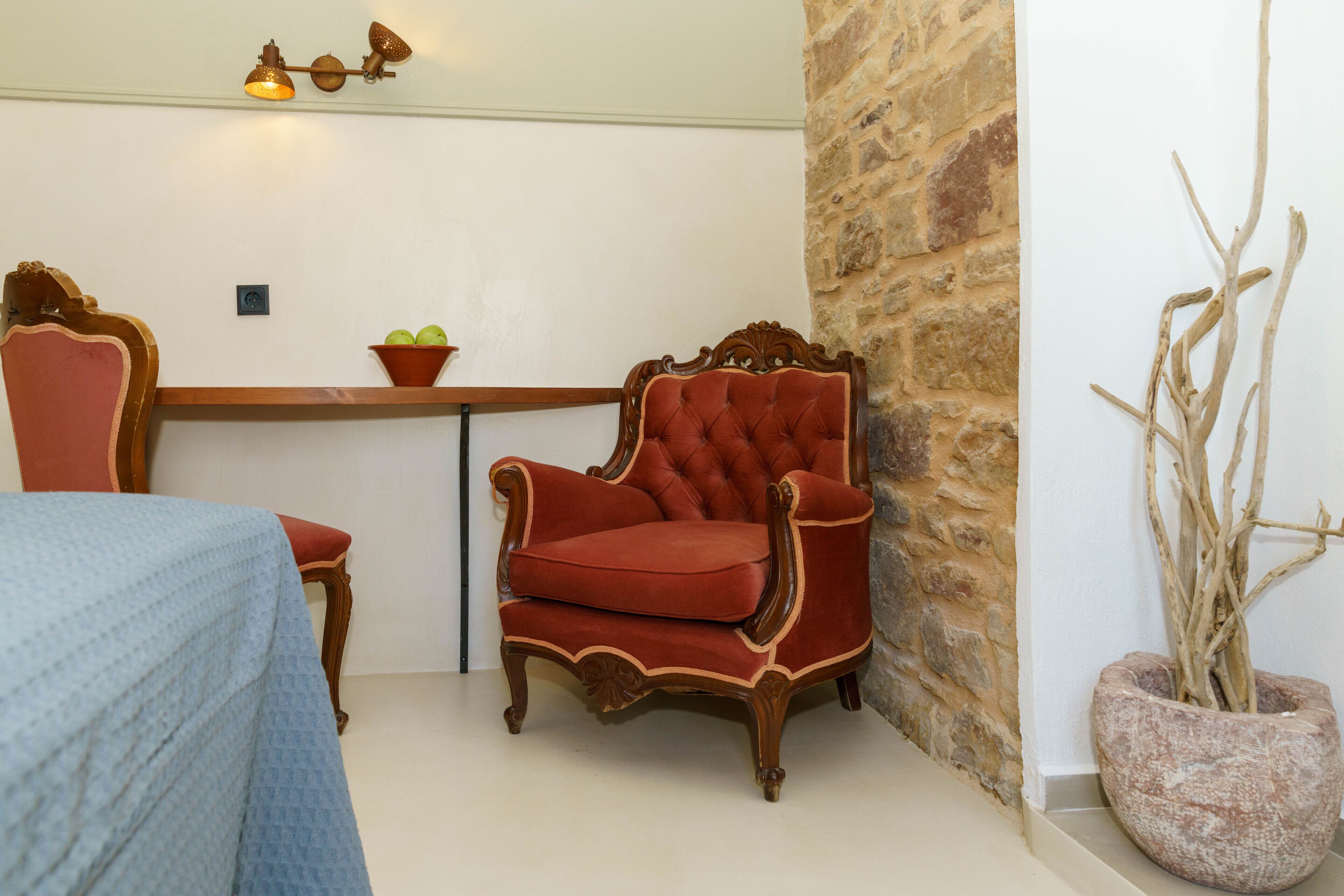 A room with a red upholstered armchair, a wooden side table with a bowl of fruit, and a potted plant.