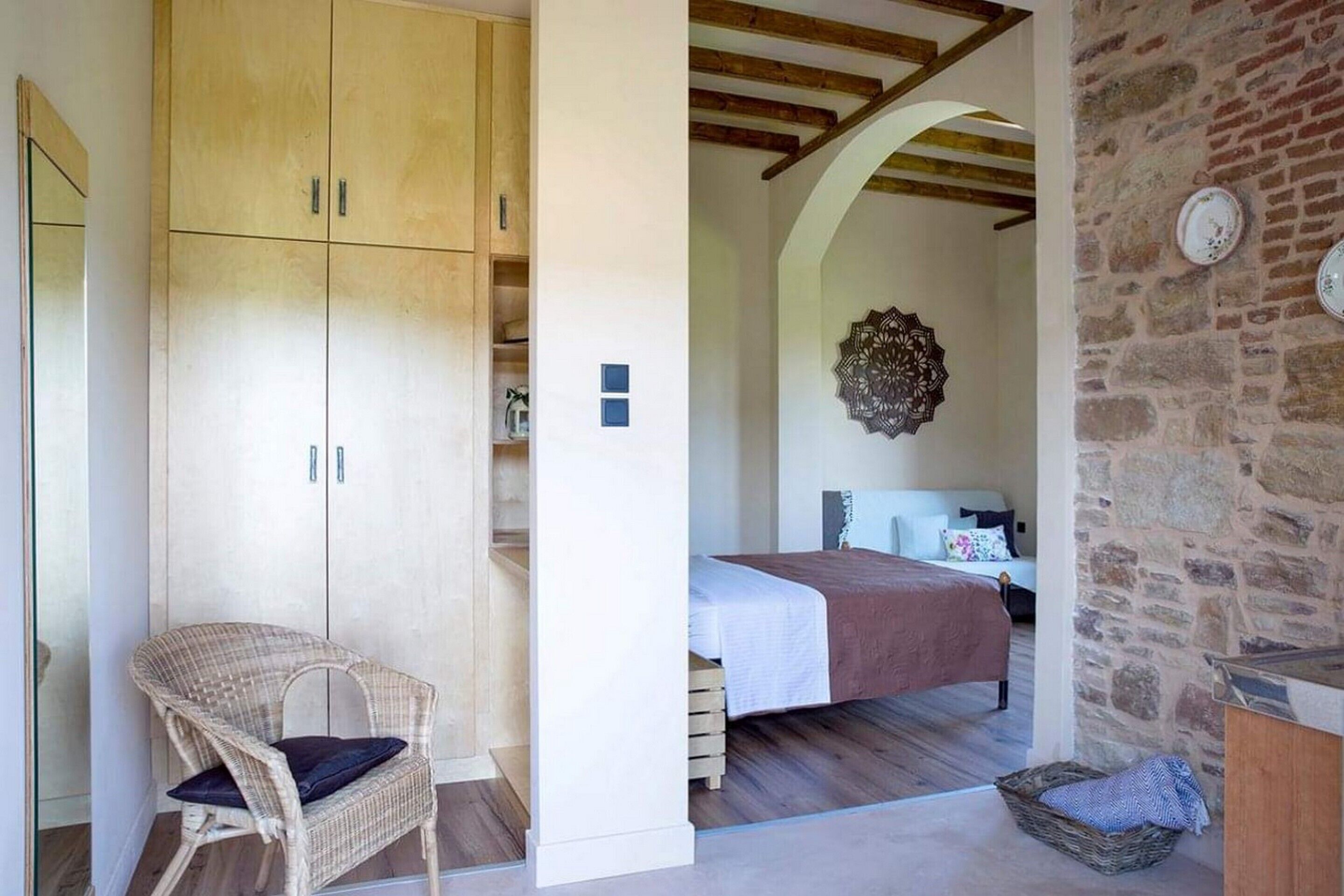 Un dormitorio con cama, una silla de mimbre, pared de piedra y techo de madera.