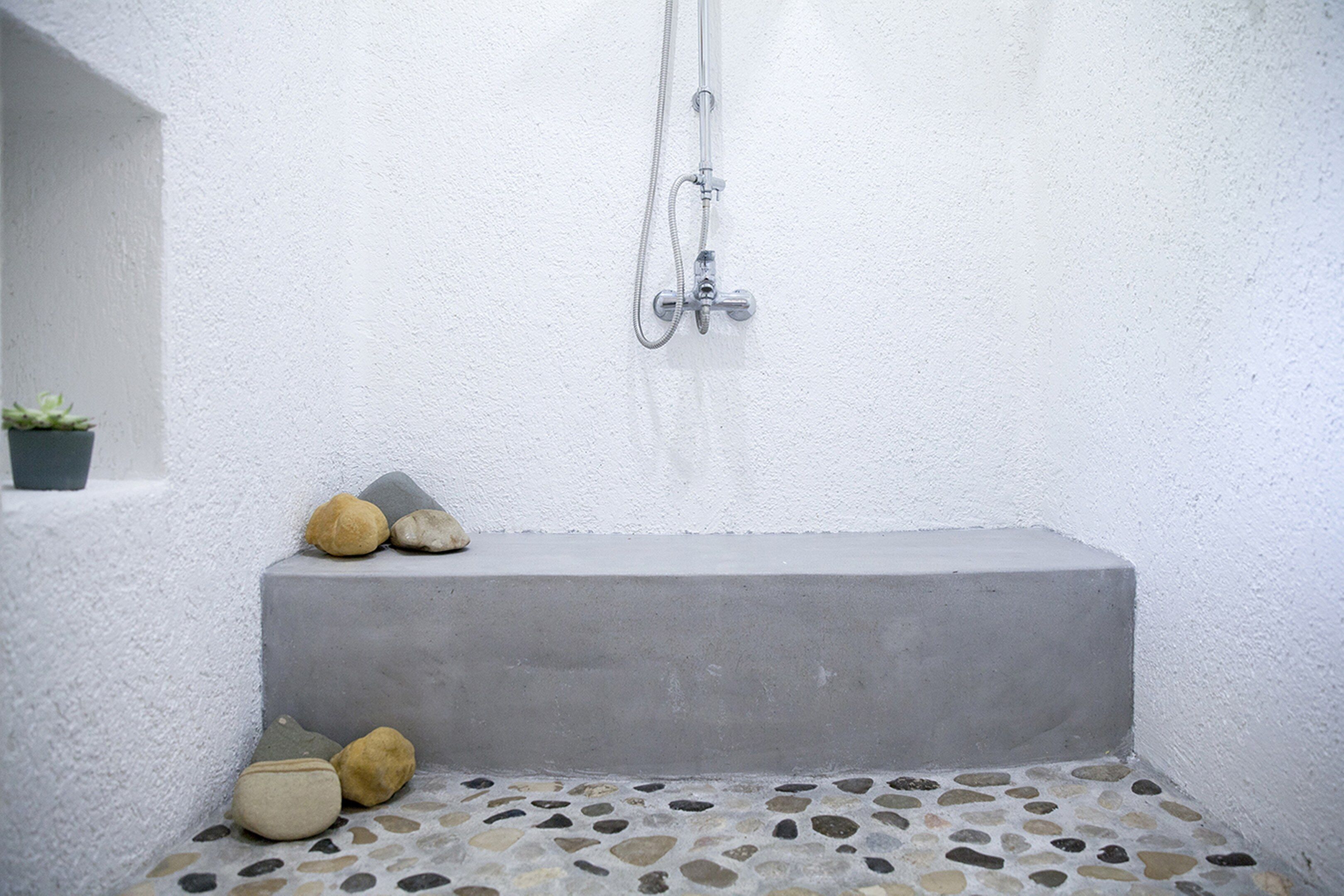 A small, enclosed shower area with a concrete bench, a stone-tiled floor, and a potted plant.