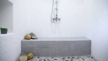 A small, enclosed shower area with a concrete bench, a stone-tiled floor, and a potted plant.
